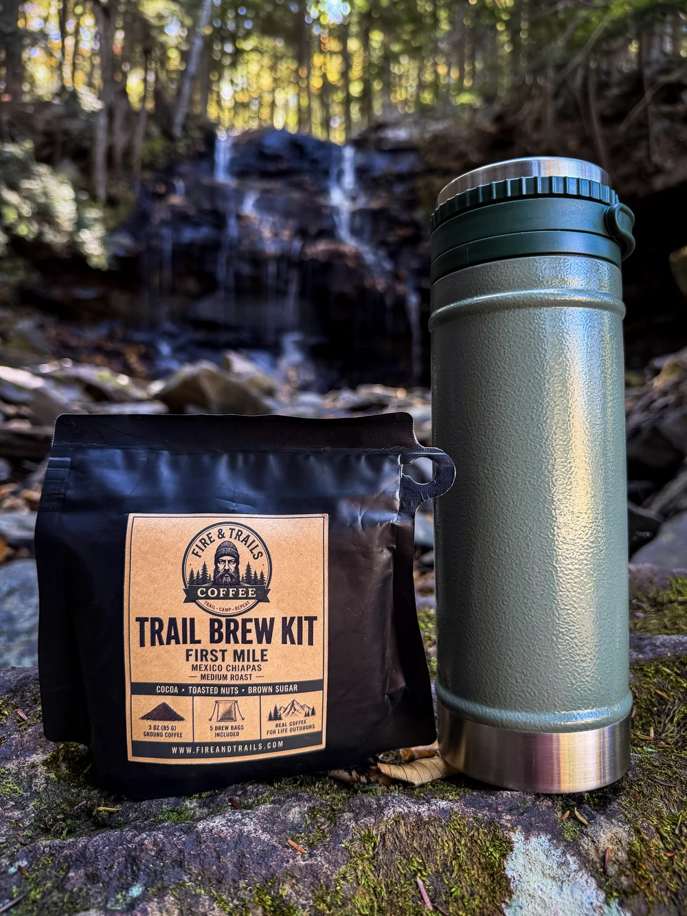 Trail Brew Kit and a green thermos on a mossy rock beside a waterfall