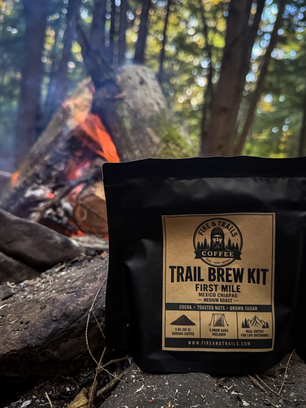 Trail Brew Kit on a log beside a glowing campfire in the woods