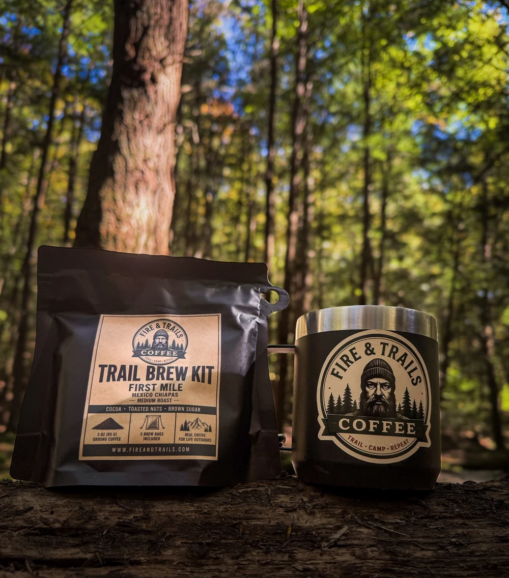 Trail Brew Kit beside a branded Fire & Trails mug on a log in the woods